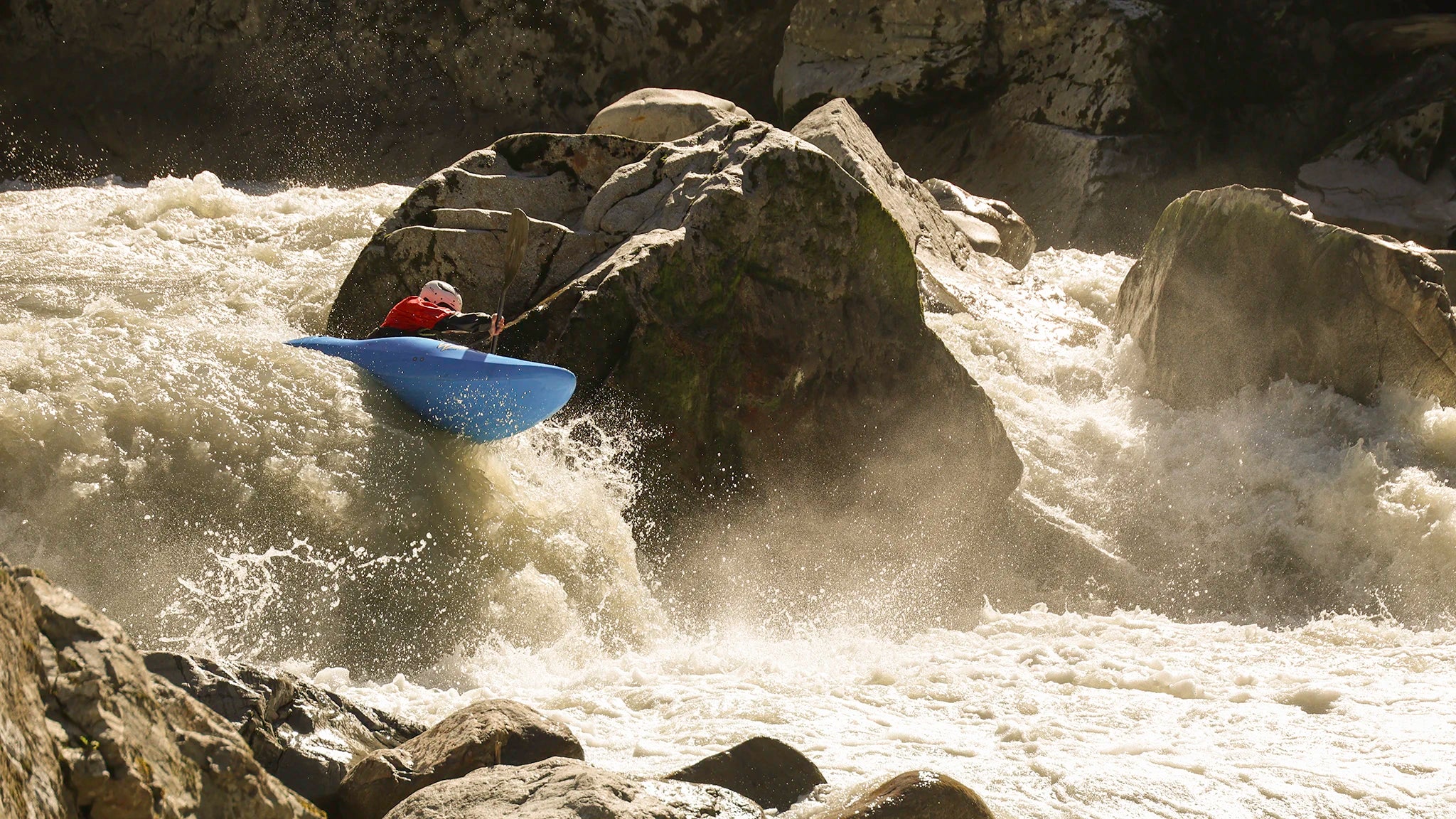 Kayaker in a blue Waka OG is boofing with a left-hand boof over a about 2 m drop on the Wellerbrücke section of the Ötztaler Ache.